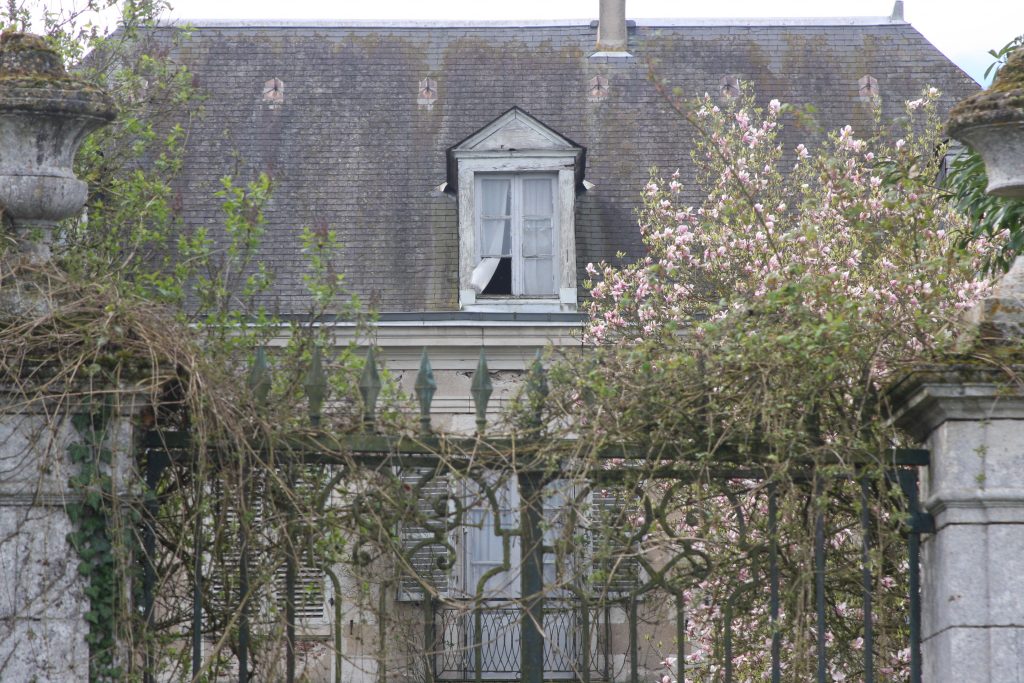 Blick durch ein Gartentor auf ein Gaubenfenster einer Villa