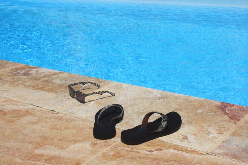 Schwarze Flipflops und Sonnenbrille am Poolrand abgelegt