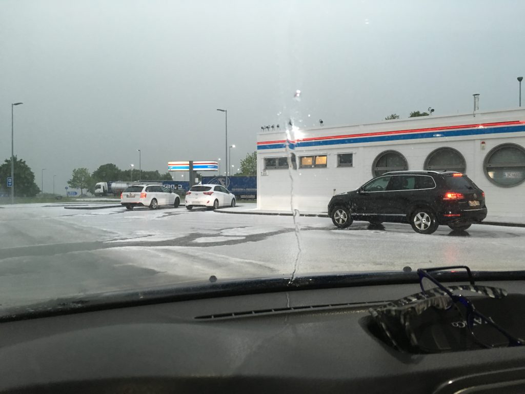Blick auf eine Autobahnraststätte, Autos und Fahrbahn mit einer Hagelkörnerschicht bedeckt